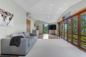 a living room with a gray couch and windows at Beachside Luxury - Laingholm Holiday Apartment in Titirangi