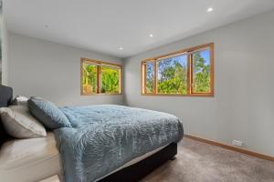 a bedroom with a bed and two windows at Beachside Luxury - Laingholm Holiday Apartment in Titirangi