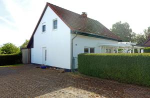 a white house with a brown roof and a hedge at Haus Sonneneck in Kaltenhof