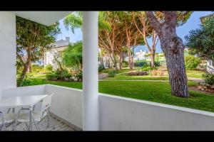 einen weißen Tisch und Stühle in einem Garten mit einem Baum in der Unterkunft Falésia Modern Flat W/Balcony & Pool by LovelyStay in Albufeira