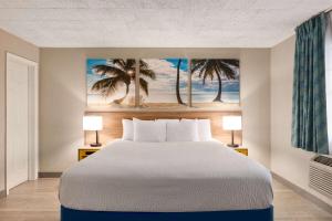 a bed in a room with two lamps and a painting of palm trees at Days Inn by Wyndham Miami Airport North in Miami