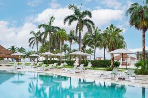 uma piscina com cadeiras e guarda-sóis e palmeiras em Hyatt Ziva Riviera Cancun All-Inclusive em Puerto Morelos