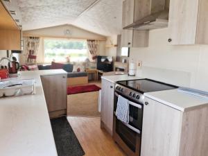 a kitchen with a stove and a living room at Lakeside Cotswold Holiday Home in Cirencester