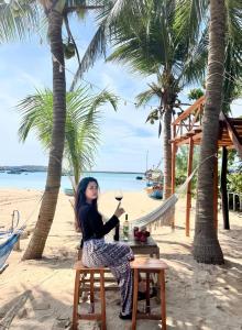una donna seduta a un tavolo sulla spiaggia con un bicchiere di vino di Mộc Homestay Đảo Phú Quý a Cu Lao Thu