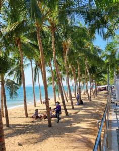 people are sitting on the beach under palm trees at Happy Beach Jomtien Guesthouse in Jomtien Beach