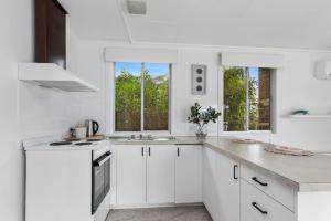 een witte keuken met witte kasten en ramen bij Great Ocean Road Sandy Villa in Apollo Bay
