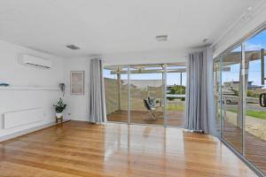 een lege woonkamer met glazen deuren en houten vloeren bij Great Ocean Road Sandy Villa in Apollo Bay
