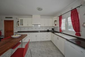 カラ・エン・ブラネスにあるVilla Savannaのキッチン(白いキャビネット、テーブル、赤いカーテン付)