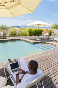 un hombre sentado en una silla con un ordenador portátil junto a una piscina en Palacio del Sol Luxury Apartments en Nafplio