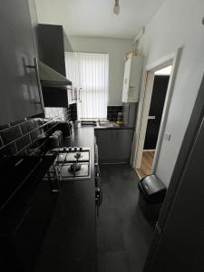La cuisine est équipée de placards noirs et d'un four avec plaques de cuisson. dans l'établissement Leeds Serviced Accommodation, à Killingbeck