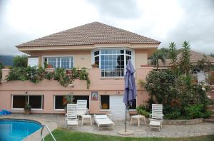 a house with a pool and chairs and a umbrella at Luxury Villa with Pool Sea and Mountain Views in Puerto de la Cruz in La Orotava