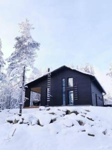 a small black house with snow on the ground at Villa Aurinkorinne Himos in Jämsä