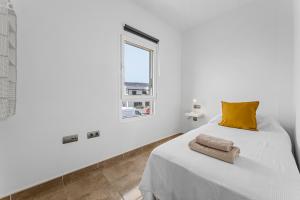ein weißes Schlafzimmer mit einem Bett mit einem gelben Kissen und einem Fenster in der Unterkunft Apartamento Arcoiris in Arrieta