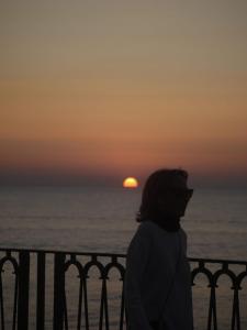 d'une femme debout sur un balcon en admirant le coucher du soleil dans l'établissement Suite ortigia vista mare, à Syracuse