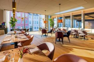 un restaurante con mesas y sillas de madera y ventanas grandes en NH Collection Copenhagen en Copenhague