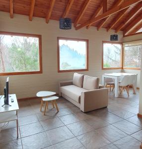 ein Wohnzimmer mit einem Sofa, Tischen und Fenstern in der Unterkunft Cabaña Victoria I in San Martín de los Andes