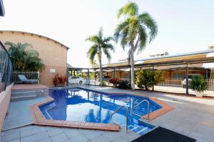 a large swimming pool with palm trees and a building at Windmill Motel & Events Centre in Mackay