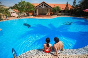 two people sitting in the pool looking at dolphins in the water at Kega Lighthouse Resort Bình Thuận in Ke Ga