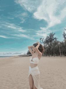 a woman in a white dress standing on the beach at Kega Lighthouse Resort Bình Thuận in Ke Ga