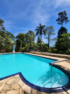 una piscina con agua azul y árboles en el fondo en POUSADA CANA DO REINO, en Embu