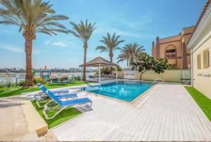 a swimming pool with two blue chairs and palm trees at Pristine Paradise Villa In Palm Jumeirah in Dubai