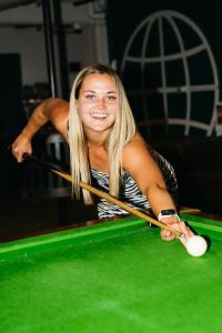 Eine Frau spielt Billard mit einem Queue auf einem Billardtisch in der Unterkunft The Village Hostels Canberra in Canberra