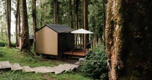 Tenjo的住宿－Bobocabin Baturraden, Purwokerto，树林中的小屋,配有桌子和雨伞