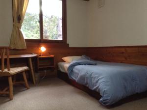 a bedroom with a bed and a desk and a window at Inn Wataboshi in Hakuba