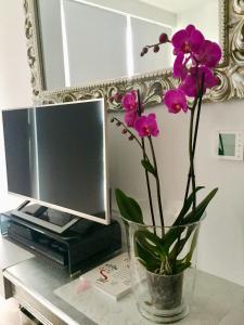 a vase with purple flowers on a table with a tv at Lelle Marine Resort Voila Apartman in Balatonlelle