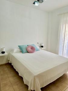 een witte slaapkamer met een groot bed met blauwe en roze kussens bij Apartamento E&D in Nerja