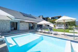 a swimming pool with umbrellas and a house at Clifton Sunset, Does have Power! in Cape Town