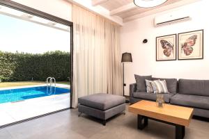 un soggiorno con divano, tavolo e piscina di Oresteia Exclusive Villa, a Sublime Retreat, By ThinkVilla a Tragaki