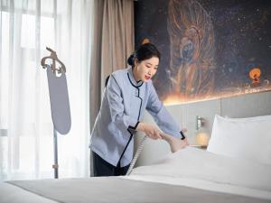 LanOu Hotel Lhasa Municipal Government Tibet University في لاسا: امرأة تقوم بترتيب السرير في غرفة في الفندق