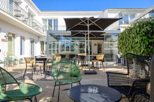 un patio con tavoli, sedie e ombrellone di Hôtel Le Martray ad Ars-en-Ré