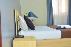 1 dormitorio con 1 cama con lámpara y almohadas en DHE Jomels Hotel, en Busia