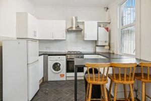 eine Küche mit weißen Geräten und einem Tisch mit Stühlen in der Unterkunft Cozy London Flat in London