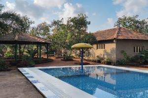 a swimming pool with an umbrella next to a house at Surve Natures Resort - Chiplun in Chiplun