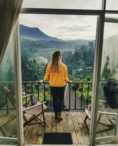 Una mujer parada en un balcón con vistas a las montañas en Waterfalls View Resort, en Talawakele