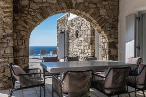 DexamenesにあるAstounding Mykonos Villa 6 Bedrooms Villa El Greco Panoramic Sea Views Facing the Ancient Island of Delos Aleomandraの石壁のパティオ(テーブル、椅子付)