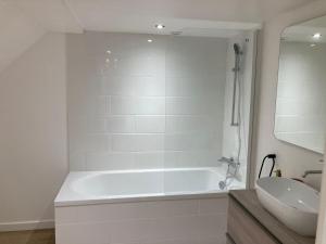 een witte badkamer met een bad en een wastafel bij Le gîte de la rue in Gréville-Hague