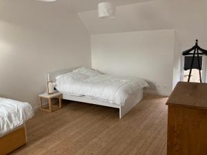 een slaapkamer met een wit bed en een houten vloer bij Le gîte de la rue in Gréville-Hague