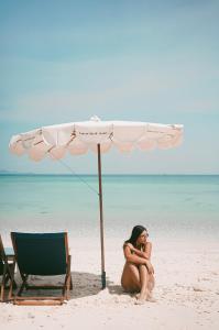 una mujer sentada bajo un paraguas en la playa en Tawaen Beach Villa, en Koh Larn