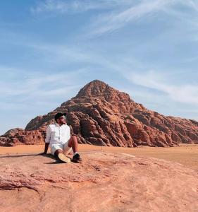 Un uomo seduto su una roccia di fronte a una montagna di Aljawhara camp and activities a Wadi Rum