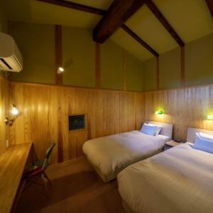 two beds in a room with wooden walls and wooden floors at ゲストハウス小布施 in Obuse