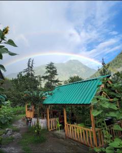 a house with a green roof with a rainbow in the background at Renuka homestay and cafe in Kasol