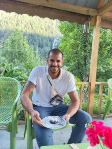 un hombre sosteniendo un plato con un pedazo de pastel en Renuka homestay and cafe, en Kasol