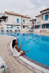 a woman sitting next to a swimming pool at Anima Jesolo - Drago Village - Family Apartments - City Center, Pool & Garden, Beach Umbrella Included, 2 Parking Spaces in Lido di Jesolo +201 photos