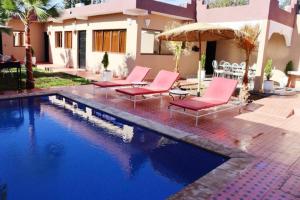 een zwembad met roze stoelen en een parasol naast een huis bij VILLA JAMAL kech in Marrakesh