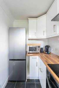 La cuisine est équipée de placards blancs et d'un réfrigérateur en acier inoxydable. dans l'établissement Quiet 2 bed flat in SW London Parking Inc, à Teddington
