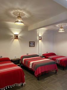três camas num quarto com lençóis vermelhos em Hotel Yubazuu em San Pablo Villa de Mitla